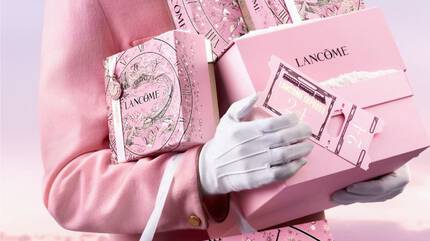 Eine Person tragt mehrere elegante Geschenkboxen von Lancome, die in dunklen Farben mit goldenen Akzenten gestaltet sind.