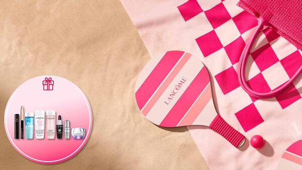 Lancome Sommer-Promotion-Banner am Strand mit einem rosa-pink gestreiften Strand-Tennisschlager und passendem Ball auf einem Handtuch im Sand. Ein runder Einleger oben rechts mit einem Geschenk-Symbol zeigt das exklusive Gratis-Geschenkset mit Lancome-Miniaturen, darunter Reinigungsprodukte wie Bi-Facil und Tonique Confort, ein Augenkajal, Mascara sowie Advanced Genifique und Renergie Pflegeprodukte.