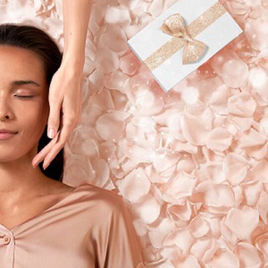 Eine Frau entspannt sich mit einer Hand im Gesicht, umgeben von hellrosa Rosenblattern und einem Geschenkpapier