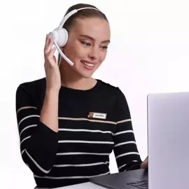 Eine lachelnde Frau mit Kopfhorern sitzt vor einem Laptop und sieht aufmerksam aus. Sie tragt ein gestreiftes Oberteil und hat ein Namensschild mit dem Namen "Laura".