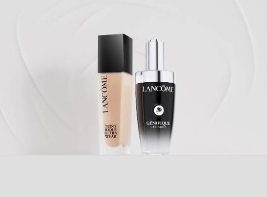 Zwei Lancome-Produkte, die Teint Idole Ultra Wear Foundation und das Genifique Ultimate Serum, stehen nebeneinander vor einem weißen Hintergrund mit subtilen grauen Wirbelmustern.