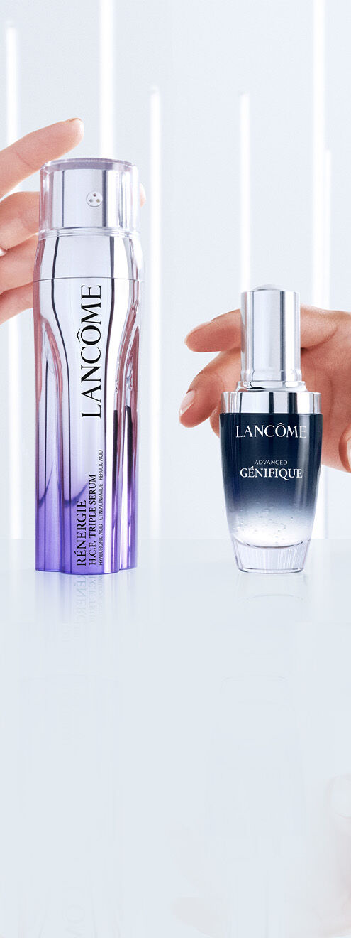 Zwei Hautpflegeprodukte der Marke Lancome, ein Serum in einer lila-flussigen Flasche und ein weiteres Serum in einer dunklen Flasche, gehalten von Handen.