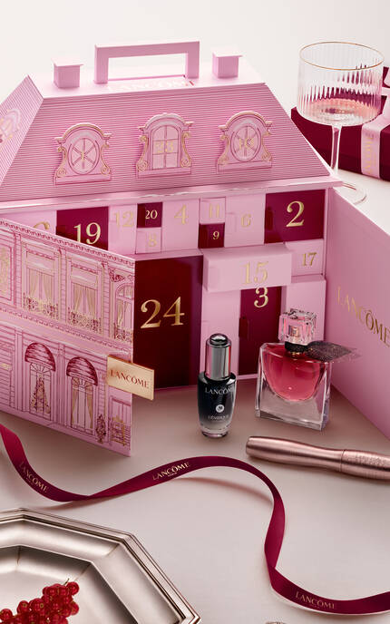 Eine Person tragt mehrere elegante Geschenkboxen von Lancome, die in dunklen Farben mit goldenen Akzenten gestaltet sind.
