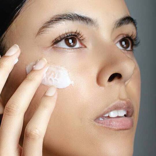 Dekoratives Bild: Nahaufnahme einer Frau, die mit ihren Fingern eine Creme unterhalb der Augenpartie auftragt