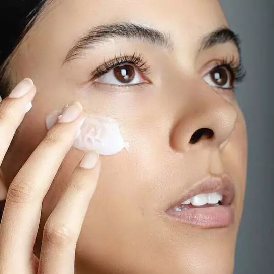 Dekoratives Bild: Nahaufnahme einer Frau, die mit ihren Fingern eine Creme unterhalb der Augenpartie auftragt