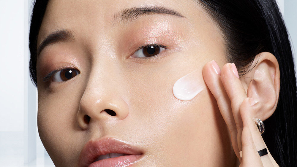 Eine Person mit glatter Haut tragt eine Gesichtspflegecreme auf die Wange auf.