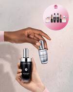 Hande halten Lancome Genifique Seren neben einem Geschenk-Symbol mit einem Aktions-Set auf der rechten Seite.