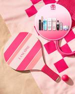 Lancome Sommer-Promotion-Banner am Strand mit einem rosa-pink gestreiften Strand-Tennisschlager und passendem Ball auf einem Handtuch im Sand. Ein runder Einleger oben rechts mit einem Geschenk-Symbol zeigt das exklusive Gratis-Geschenkset mit Lancome-Miniaturen, darunter Reinigungsprodukte wie Bi-Facil und Tonique Confort, ein Augenkajal, Mascara sowie Advanced Genifique und Renergie Pflegeprodukte.