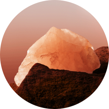 Ein glitzernder, rosa Kristall ruht auf einer moosbedeckten Felsoberflache vor einem sanften, orangefarbenen Hintergrund.