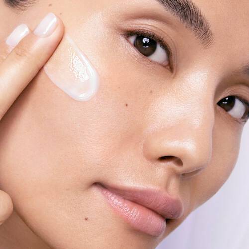 Nahaufnahme einer Person, die ein leichtes, transparentes Serum auf ihre Wange auftragt.