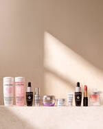 Eine Auswahl an Lancome-Beauty- und Pflegeprodukten, darunter Lait Galatee Confort, Tonique Confort, Genifique Ultime, Renergie-Cremes, ein Lippenstift und ein La Vie Est Belle Parfum, prasentiert auf einer hellen, strukturierten Oberflache.