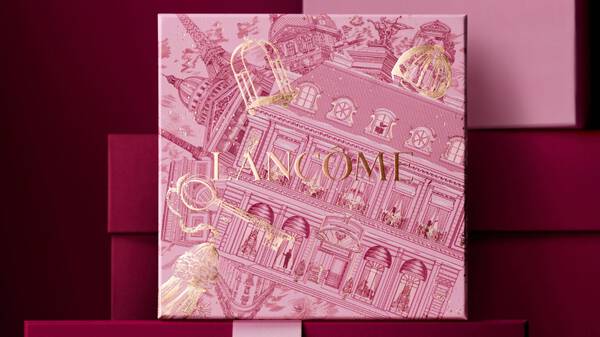Rosa Lancome-Geschenkbox mit festlichem Muster vor einem burgunderroten Hintergrund.