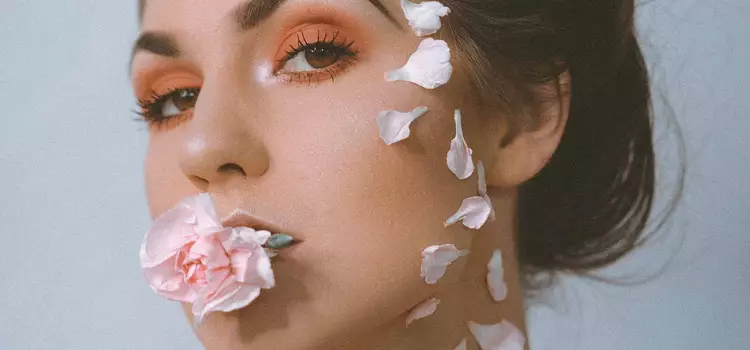 Frau mit rosa Blutenblattern im Gesicht und Rose im Mund