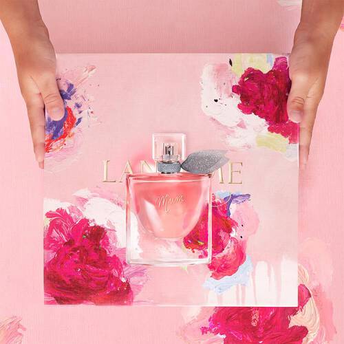 Hande halten eine Parfumflasche auf einer kunstvoll gestalteten Verpackung mit rosa und blauen Blumenmotiven.