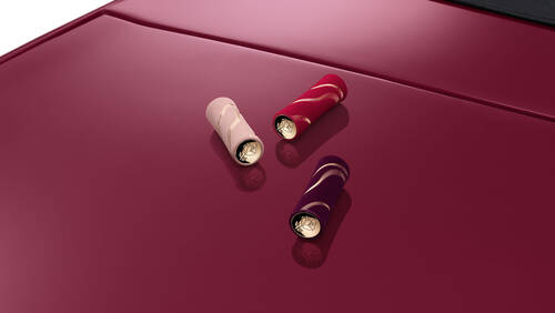 Drei elegante Schalen in Rosa, Lila und Rot auf der glanzenden Motorhaube eines burgunderfarbenen Autos.
