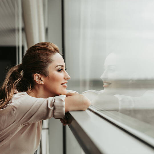 Dekoratives Bild: Frau im Seitenprofil, die lachelnd aus einem Fenster schaut
