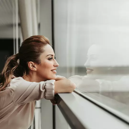 Dekoratives Bild: Frau im Seitenprofil, die lachelnd aus einem Fenster schaut