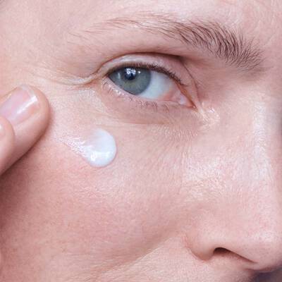 Frau tragt Creme unter ihrem Auge auf