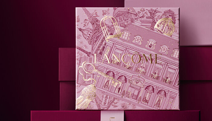 Rosa Lancome-Geschenkbox mit festlichem Muster vor einem burgunderroten Hintergrund.