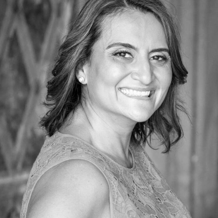 Eine lachelnde Frau mit lockigem Haar, die in einem lassigen, eleganten Outfit posiert, vor einem stilvollen Hintergrund.