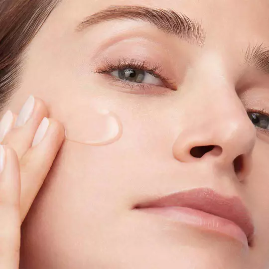 Nahaufnahme einer Frau, die ein transparentes, gelartiges Hautpflegeprodukt auf ihre Wange auftragt.