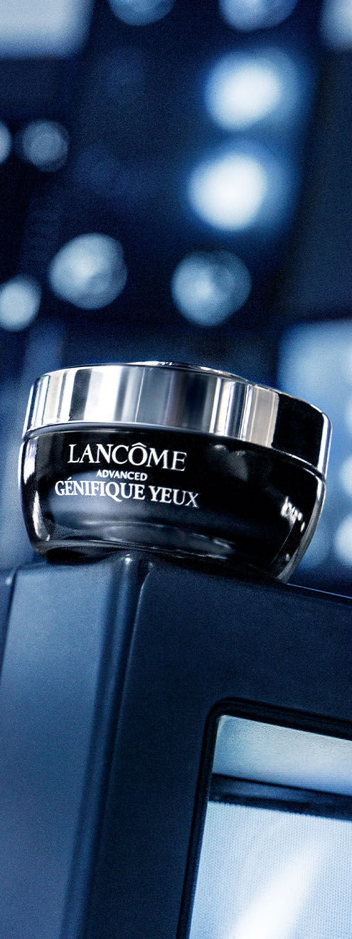 Ein Glas Tiegel mit der Aufschrift "Lancome Advanced Genifique Yeux" steht auf einem Bildschirm. Der Hintergrund ist dunkel und unscharf.