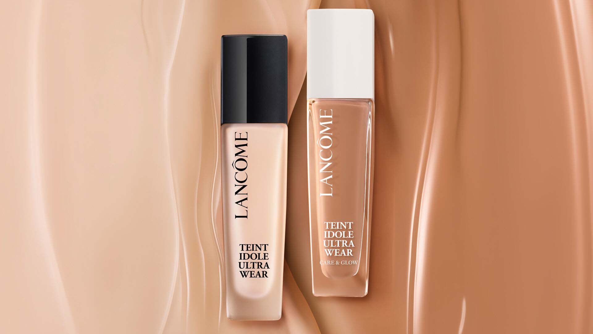 Zwei Flaschchen Foundation von Lancome, Teint Idole Ultra Wear, auf einem Hintergrund aus sanften Hauttonen.
