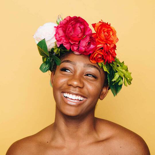 Frau mit strahlender, straffer Haut und buntem Blumenkranz auf dem Kopf