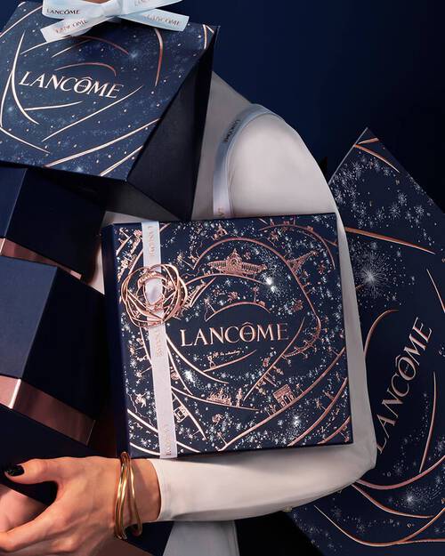 Eine Person halt mehrere festlich verpackte Lancome-Geschenkkartons in dunklem Blau mit glitzernden Sternenmotiven.