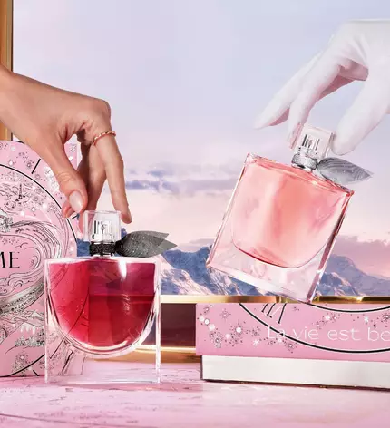 Eine Person tragt mehrere elegante Geschenkboxen von Lancome, die in dunklen Farben mit goldenen Akzenten gestaltet sind.