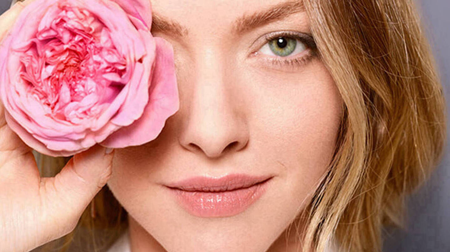 Eine Frau verdeckt mit einer Blume ihr rechtes Auge und lachelt.