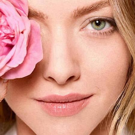 Eine Frau verdeckt mit einer Blume ihr rechtes Auge und lachelt.