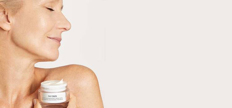 Frau in den Wechseljahren mit geschlossenen Augen halt die Nutrix Face Cream in die Kamera.