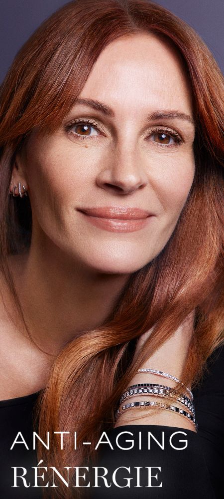Nahaufnahme von Julia Roberts mit rotbraunem Haar, die mehrere Armbander tragt, mit dem Text "ANTI-AGING RENERGIE" unten.