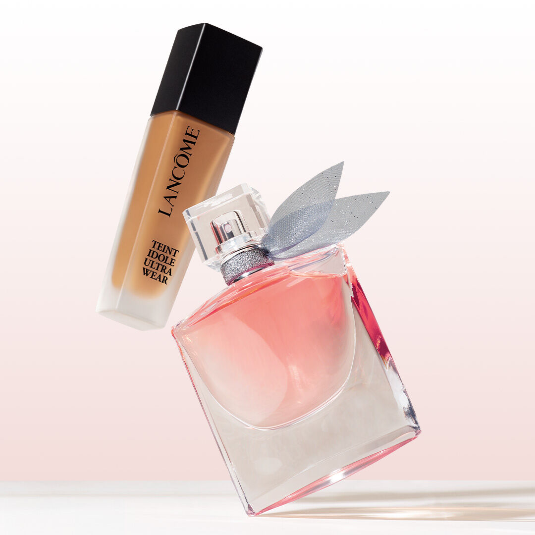 Eine Flasche Lancome Foundation und ein Parfum mit Schleife, vor einem sanften, blassen Hintergrund.