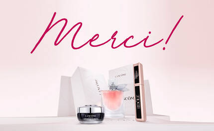 Alt-Text: Eine stilvolle Anordnung von Lancome-Produkten, darunter ein Parfum, eine Creme und eine Mascara, mit dem Schriftzug "Merci!" in pinker Farbe im Hintergrund.