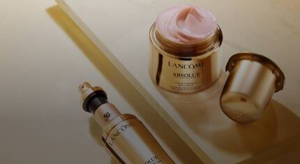 Alt-Text: Zwei Produkte von Lancome aus der Absolue-Serie: ein Serum mit Pumpspender und eine Creme in einem eleganten Glasbehalter, beide in goldenen Verpackungen auf einem hellen Hintergrund.
